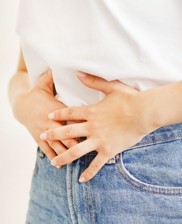 Kobieta w białej bluzce trzymająca się za brzuch